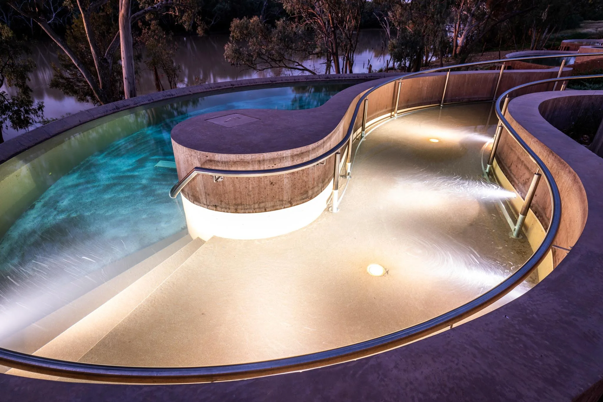 A lit riverside pool at dusk, architectural photography by Gerkies
