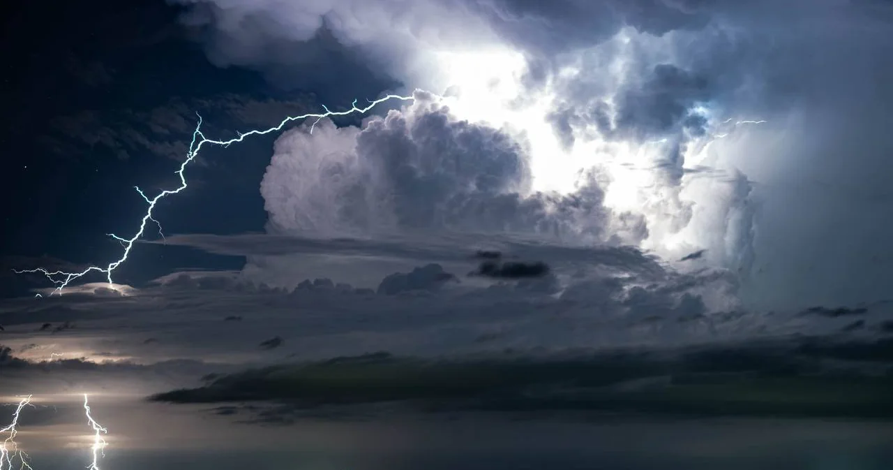 Branching lightning crosses dark storm clouds, with bright bolts near the horizon