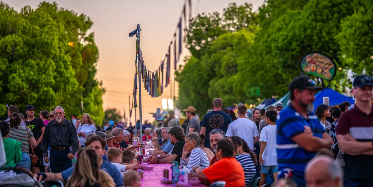 Guests along the long table at dusk under strings of flags